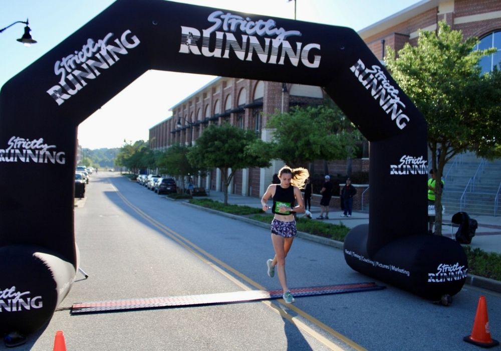 Runner crossing finish line checking watch — 2026 Strides for Autism